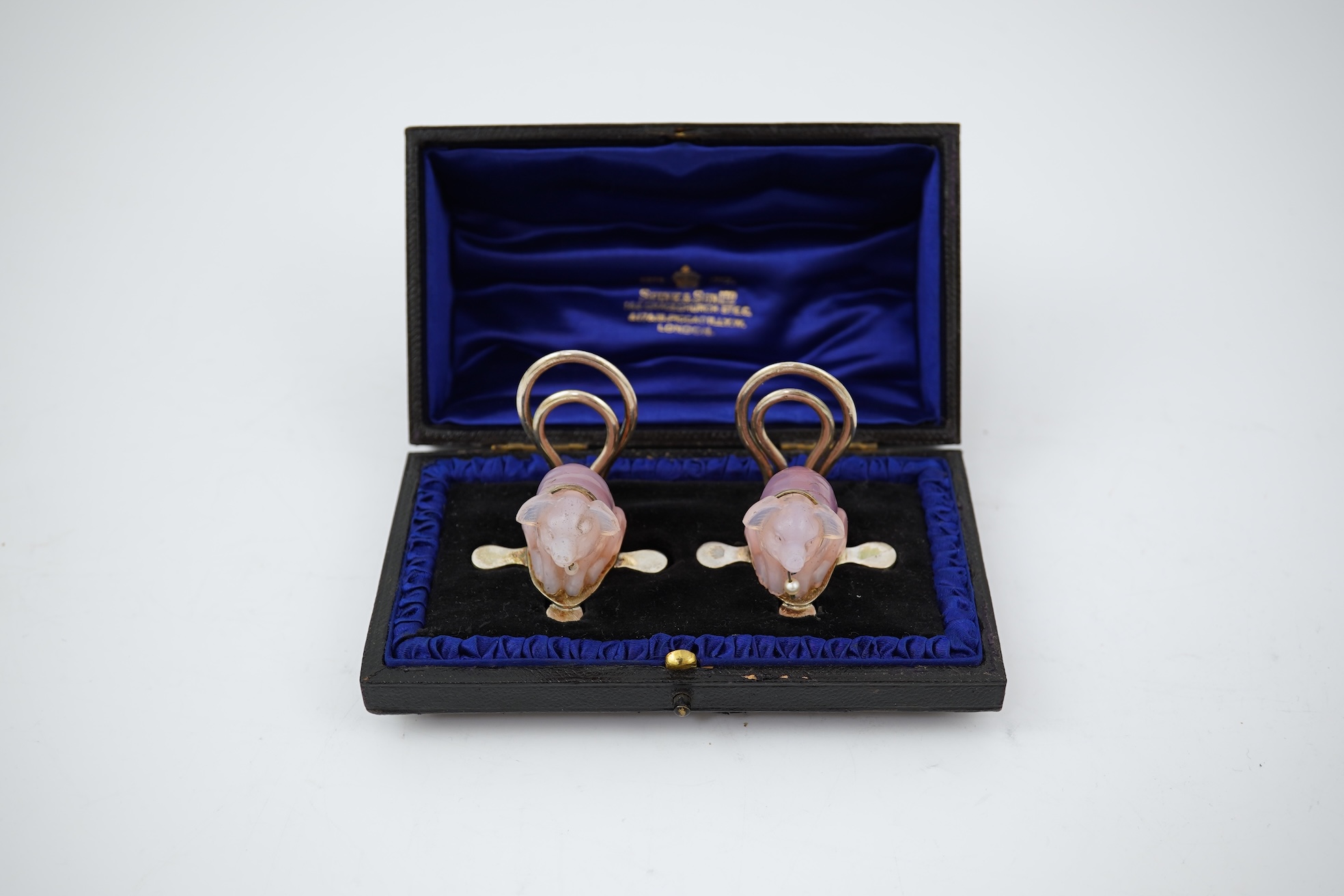 A cased pair of unusual Edwardian silver and pink glass mounted menu holders, by William Comyns, each modelled as a seated pig with collar